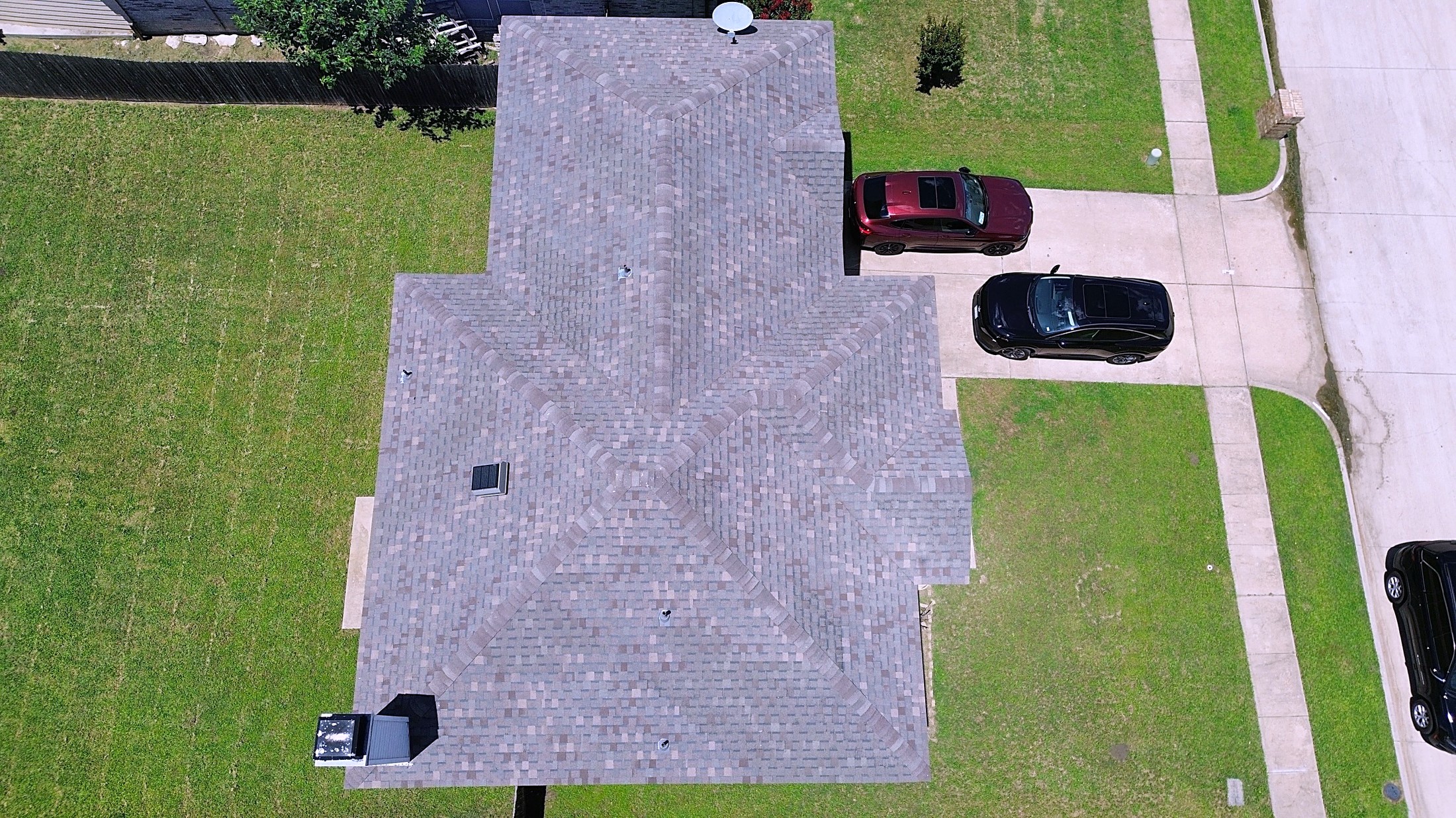 A grey shingle roof on a brick ranch house among mature trees